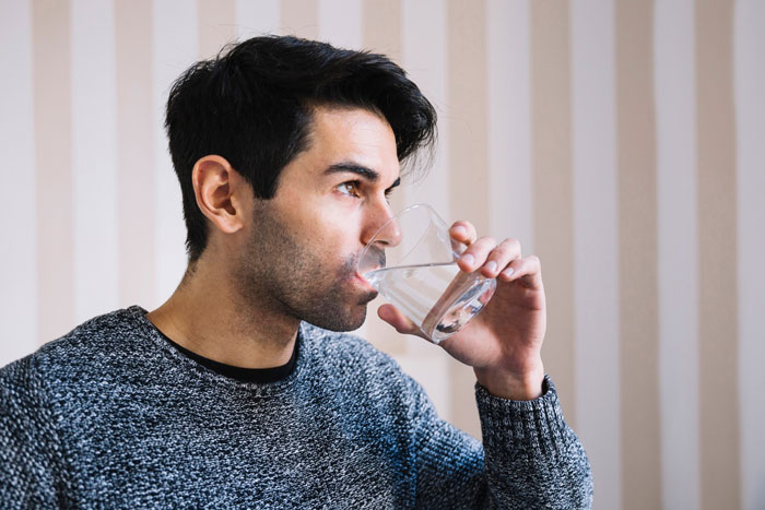 Man drinking sparkling water from a glass with a contemplative expression, near striped wallpaper. Man drinking sparkling water from a glass with a contemplative expression, near striped wallpaper.