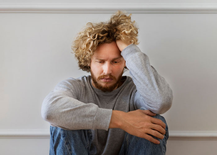 Man with curly hair sitting pensively on the floor, contemplating sparkling water preferences. Man with curly hair sitting pensively on the floor, contemplating sparkling water preferences.