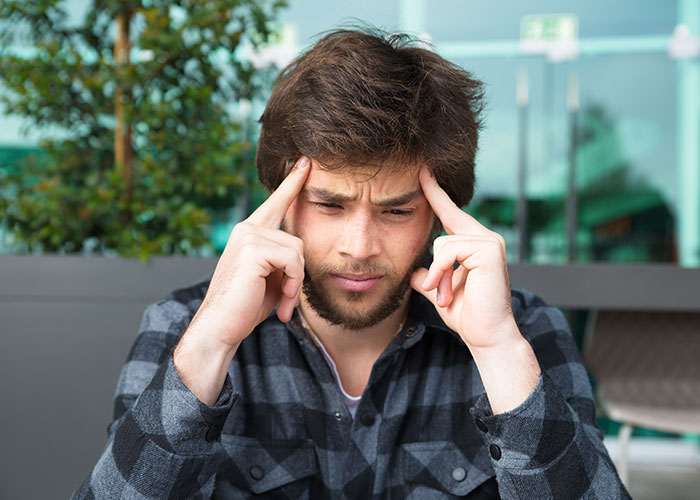 Man in plaid shirt looking stressed, contemplating about faking an allergy, outdoors with greenery in the background. Man in plaid shirt looking stressed, contemplating about faking an allergy, outdoors with greenery in the background.