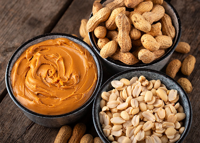 Peanuts and peanut butter displayed in bowls on a wooden surface. Peanuts and peanut butter displayed in bowls on a wooden surface.