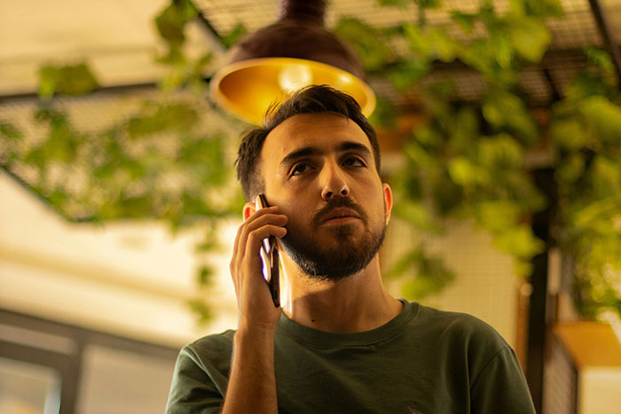 Man with beard talking on phone indoors, appearing serious, relating to hubby confronting family about pregnant wife treatment. Man with beard talking on phone indoors, appearing serious, relating to hubby confronting family about pregnant wife treatment.