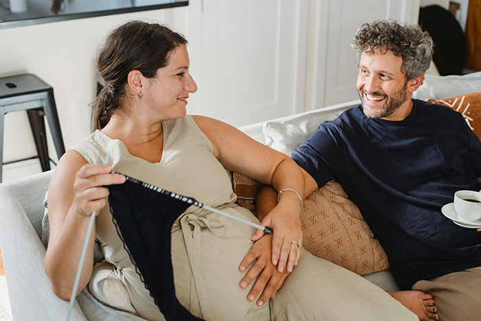 Pregnant woman knitting on sofa while husband smiles, reflecting family tension and confrontation over treatment issues. Pregnant woman knitting on sofa while husband smiles, reflecting family tension and confrontation over treatment issues.