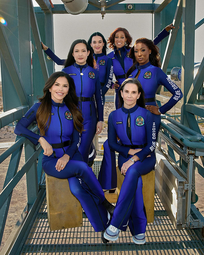 Women in Blue Origin space suits pose on a metal structure. Women in Blue Origin space suits pose on a metal structure.