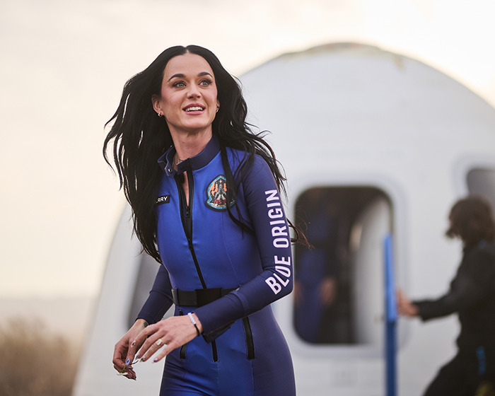 Singer in blue space outfit, smiling after space flight mission, amidst fan outrage over $175 doll. Singer in blue space outfit, smiling after space flight mission, amidst fan outrage over $175 doll.