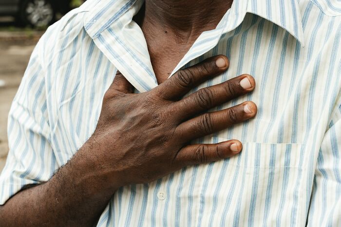 A person in a striped shirt with a hand on their chest, possibly reacting to an unexpected situation.