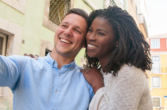 Man and woman smiling outdoors, capturing a selfie together. Man and woman smiling outdoors, capturing a selfie together.