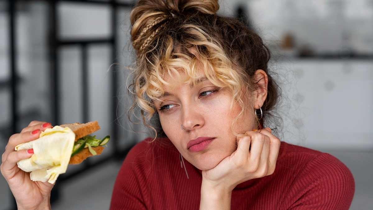 Woman holding sandwich looking displeased and bored, illustrating fiancu00e9 buys sandwich she is allergic to