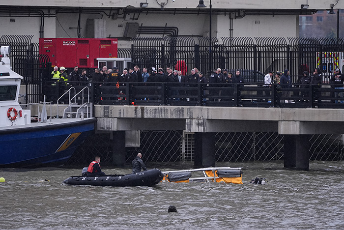 Helicopter crash scene with rescuers and onlookers by the water, highlighting eerie detail that may explain the crash. Helicopter crash scene with rescuers and onlookers by the water, highlighting eerie detail that may explain the crash.