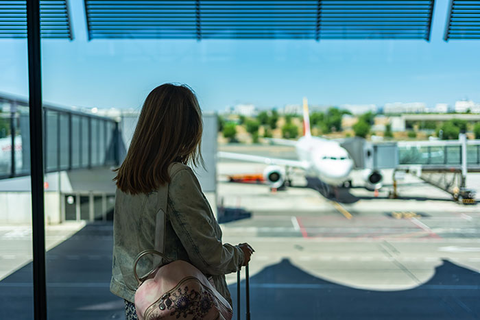 Woman at airport window with suitcase, looking at plane on runway. Woman at airport window with suitcase, looking at plane on runway.