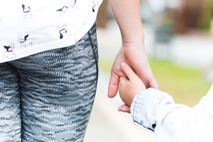 Woman holding child's hand, wearing patterned leggings, signifying babysitting trust. Woman holding child's hand, wearing patterned leggings, signifying babysitting trust.
