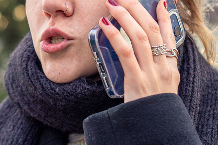 Woman on a phone call outside during winter, wearing a scarf and ring, discussing babysitting arrangements. Woman on a phone call outside during winter, wearing a scarf and ring, discussing babysitting arrangements.