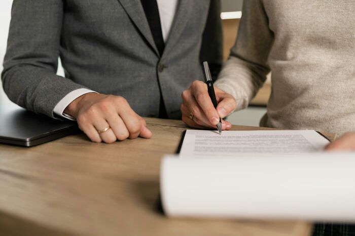 Two people at a table, one signing a document, suggesting a financial agreement or loan discussion. Two people at a table, one signing a document, suggesting a financial agreement or loan discussion.