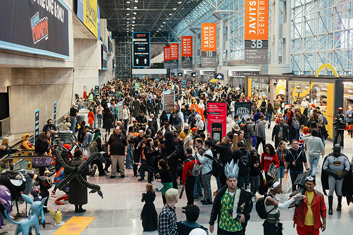 Crowded convention center with attendees in costumes and casual wear, focusing on affordable getaway over expensive wedding choice.