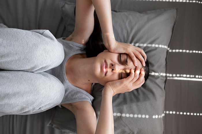 Woman in gray loungewear lying on a bed, holding her head, experiencing anxiety before a wedding. Woman in gray loungewear lying on a bed, holding her head, experiencing anxiety before a wedding.