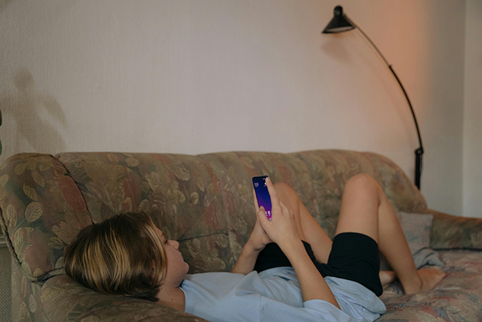 Person relaxing on a sofa, holding a phone, representing anxiety relief in a cozy home setting. Person relaxing on a sofa, holding a phone, representing anxiety relief in a cozy home setting.