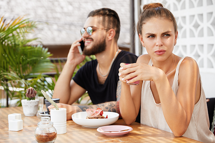 Woman looking upset holding cup, man on phone; tension over family assets and biological kids. Woman looking upset holding cup, man on phone; tension over family assets and biological kids.