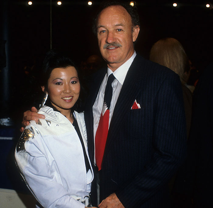 A man in a suit and woman in a white jacket pose together at an event, smiling at the camera. A man in a suit and woman in a white jacket pose together at an event, smiling at the camera.