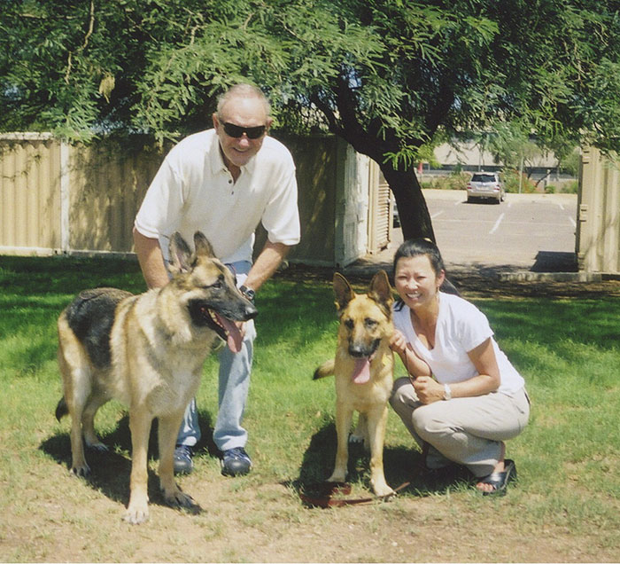 Man and woman with two German Shepherds on grass, smiling under a tree. Man and woman with two German Shepherds on grass, smiling under a tree.