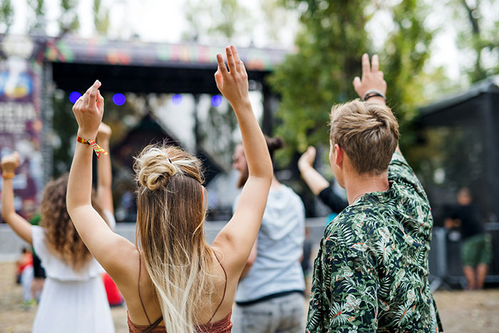 Couple enjoying an outdoor event, hands raised, with stage in the background, experiencing FOMO from friends' wedding ceremony. Couple enjoying an outdoor event, hands raised, with stage in the background, experiencing FOMO from friends' wedding ceremony.