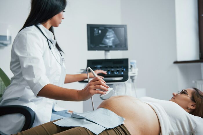 Doctor performing an ultrasound, examining patient’s abdomen in a medical setting, with focus on medical equipment.