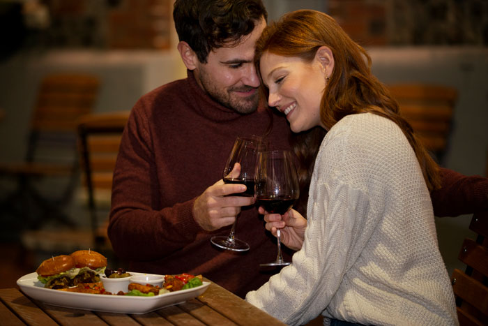 Couple on a cozy date night, smiling and clinking wine glasses at an outdoor restaurant. Couple on a cozy date night, smiling and clinking wine glasses at an outdoor restaurant.