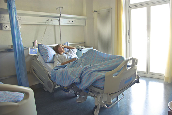 Person in hospital bed near a window, looking thoughtful with hand on head. Person in hospital bed near a window, looking thoughtful with hand on head.