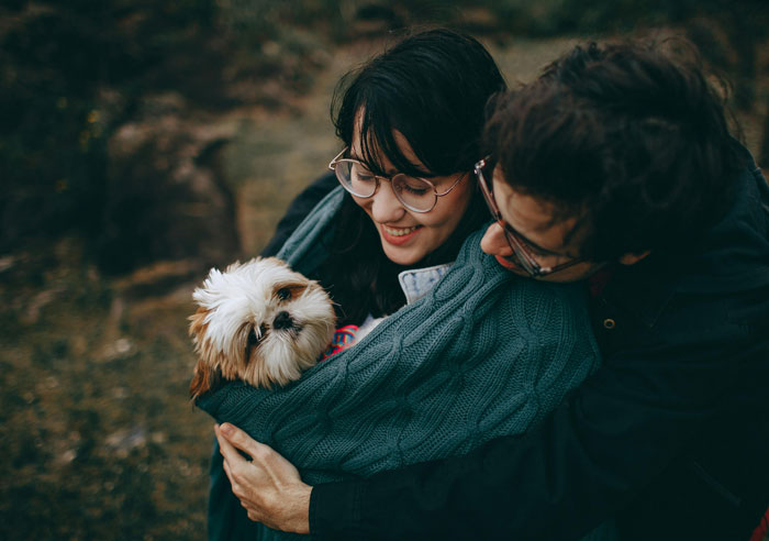 Couple with a small dog wrapped in a green blanket, outdoors. Couple with a small dog wrapped in a green blanket, outdoors.