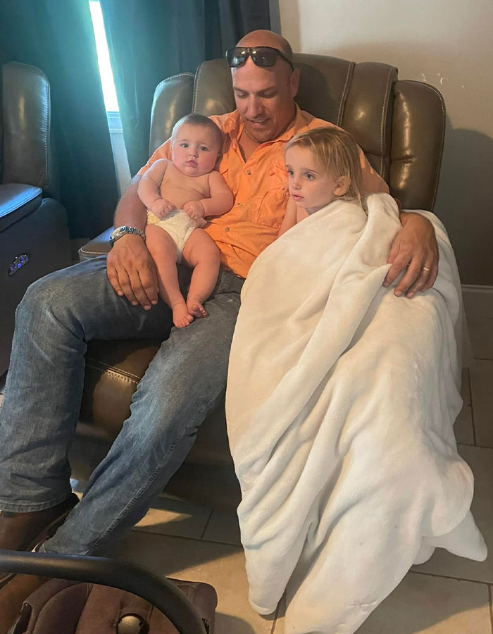 A man in an orange shirt holds two toddlers in a cozy armchair. A man in an orange shirt holds two toddlers in a cozy armchair.