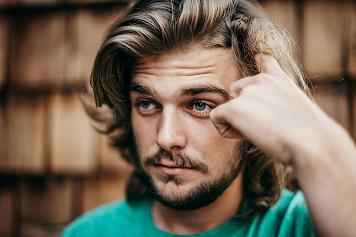 Man with long hair and beard, wearing a green shirt, taking care of his autistic cousin.