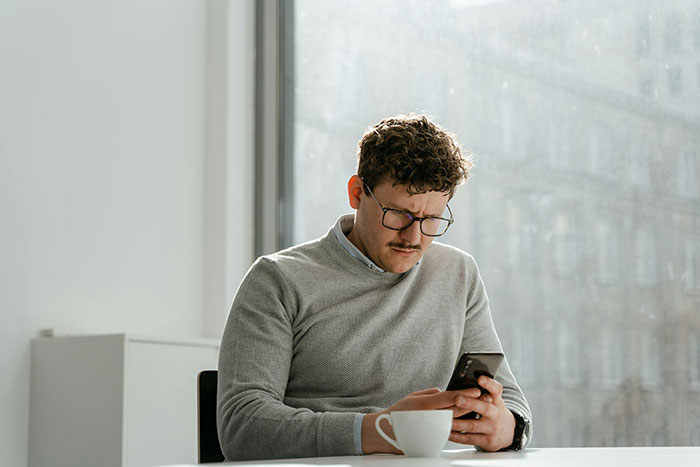 Man with glasses in a gray sweater, using phone by a window, caring attention. Man with glasses in a gray sweater, using phone by a window, caring attention.