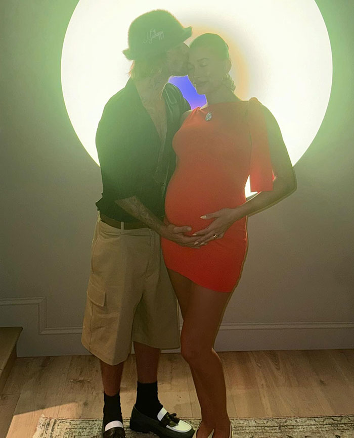 Couple in a tender moment, with one partner in a red dress, backlit by a large circular light in a cozy room. Couple in a tender moment, with one partner in a red dress, backlit by a large circular light in a cozy room.