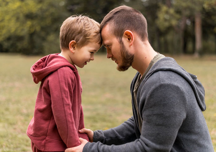 A man and child in hoodies touch foreheads affectionately in a park setting. A man and child in hoodies touch foreheads affectionately in a park setting.
