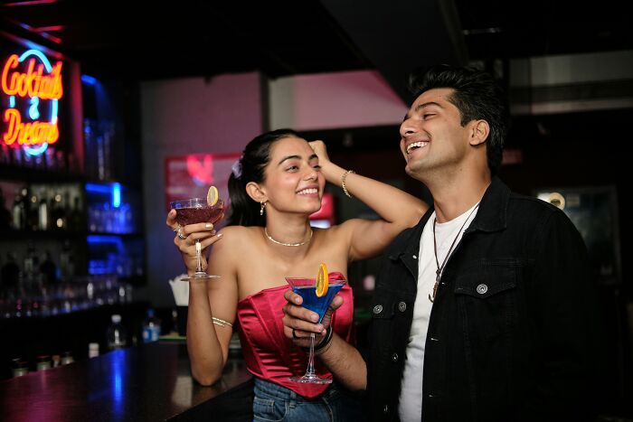 A guy and a woman enjoying cocktails at a bar, smiling and socializing, exploring why guys slept with a married woman.