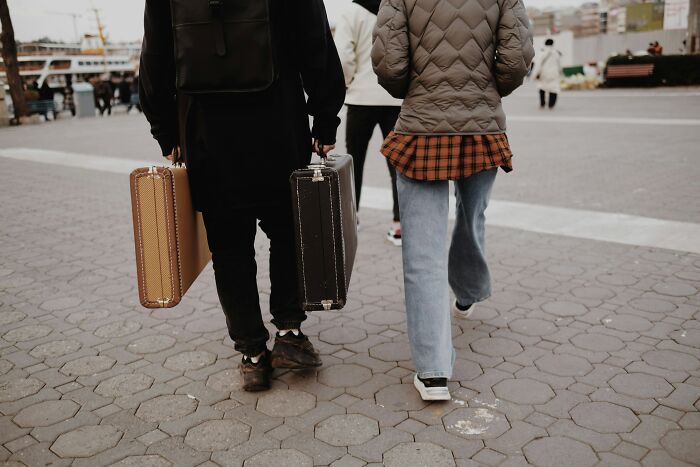 Two people carrying luggage, walking outside, hinting at a family vacation scenario. Two people carrying luggage, walking outside, hinting at a family vacation scenario.