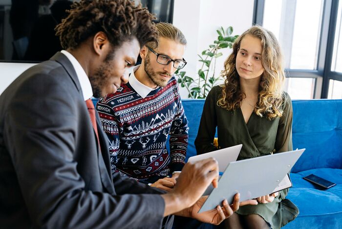 Three people discussing homeowner first-home tips with a document in a modern office setting.