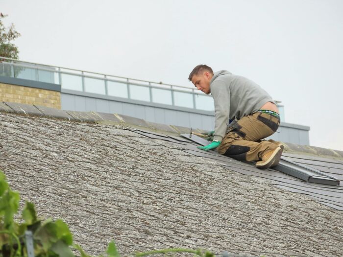 Man working on roof repairs, wearing gloves and casual attire, demonstrating tips for homeowner-first-home maintenance.
