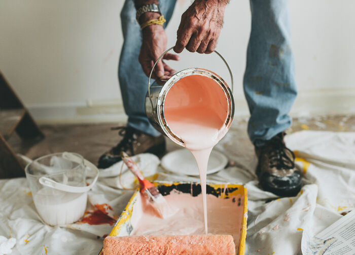 Person pouring pink paint into a tray for a DIY project, illustrating homeowner first home tips.