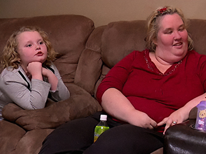 Young girl sitting on a couch next to a woman in red, both appearing relaxed. Young girl sitting on a couch next to a woman in red, both appearing relaxed.
