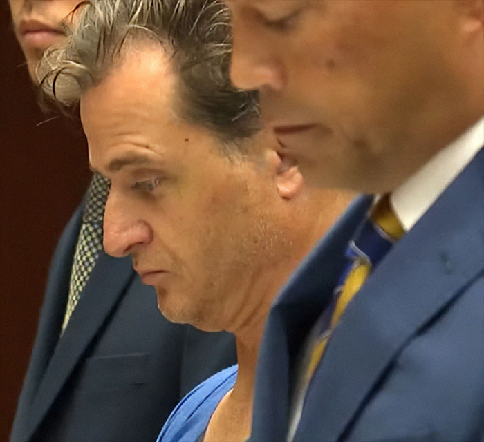 Male doctor in court, involved in alleged cliff incident with wife, appearing tense during proceedings. Male doctor in court, involved in alleged cliff incident with wife, appearing tense during proceedings.