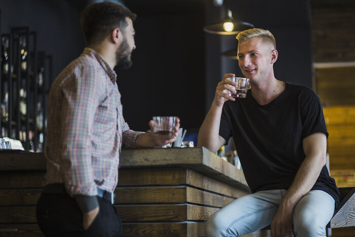 Two men drinking and talking at a bar, discussing views on parenting and roles in raising kids. Two men drinking and talking at a bar, discussing views on parenting and roles in raising kids.
