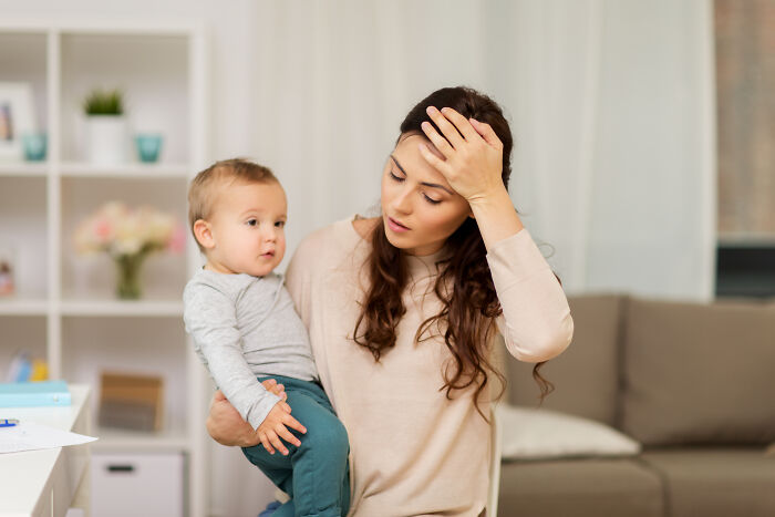 New mom looking concerned while holding baby, highlighting challenges of parenting. New mom looking concerned while holding baby, highlighting challenges of parenting.