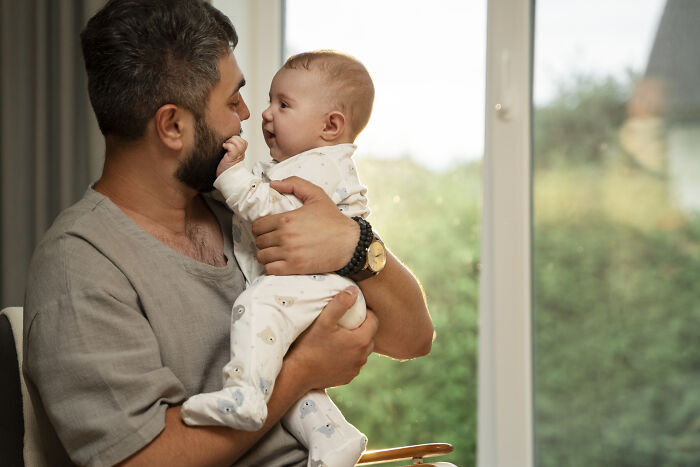 Father holding baby near window, illustrating parenting roles and challenges faced by new moms. Father holding baby near window, illustrating parenting roles and challenges faced by new moms.