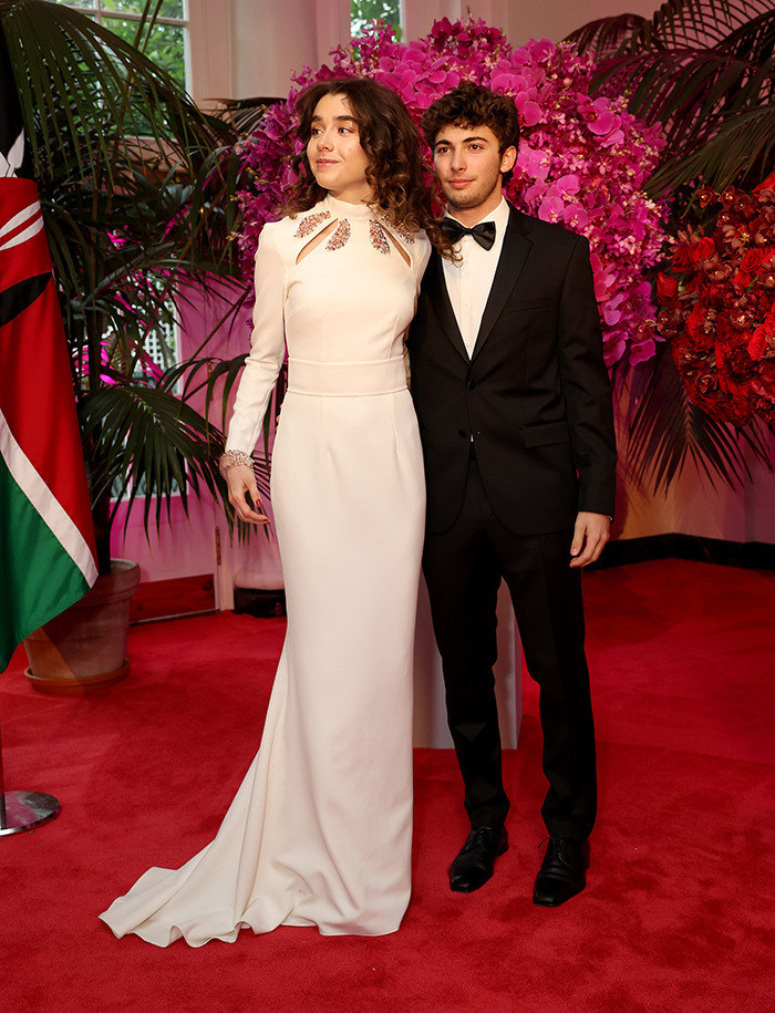 Young couple in formal attire at a glamorous event, posing by vibrant floral arrangements. Young couple in formal attire at a glamorous event, posing by vibrant floral arrangements.