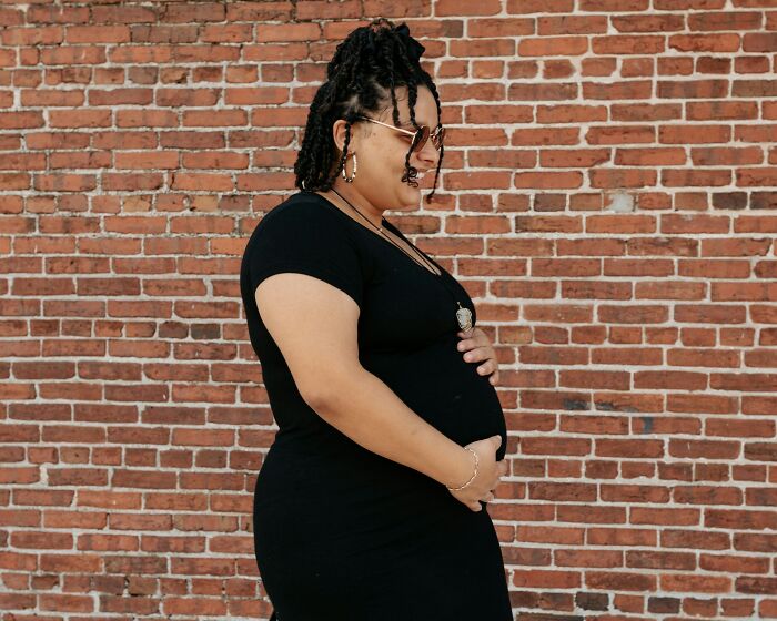 Person in a black dress against a brick wall, smiling, believed to be pranking due to April Fools' timing.