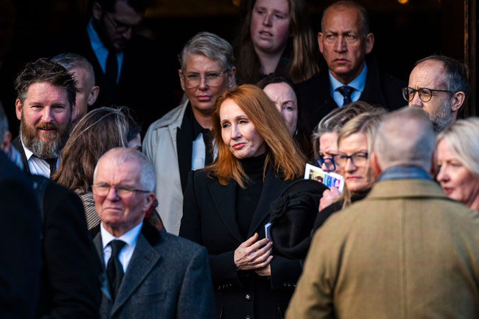 A woman with red hair stands among a group of people, wearing a black coat, after a Supreme Court ruling on trans rights. A woman with red hair stands among a group of people, wearing a black coat, after a Supreme Court ruling on trans rights.