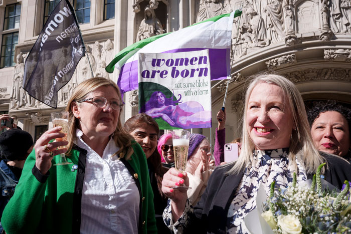 Women holding a banner and drinks outside a court, celebrating a ruling related to trans rights. Women holding a banner and drinks outside a court, celebrating a ruling related to trans rights.