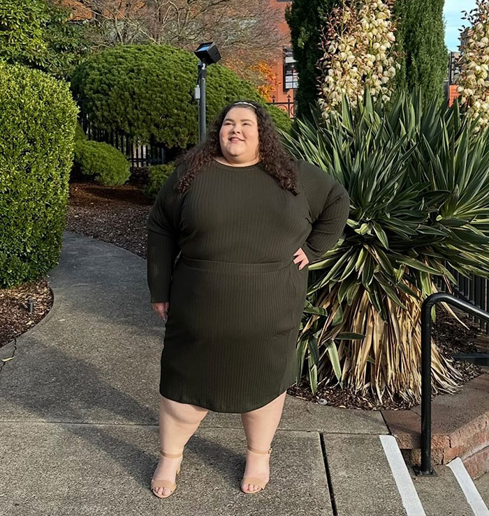 Plus-sized passenger standing outdoors in a green dress, surrounded by greenery. Plus-sized passenger standing outdoors in a green dress, surrounded by greenery.