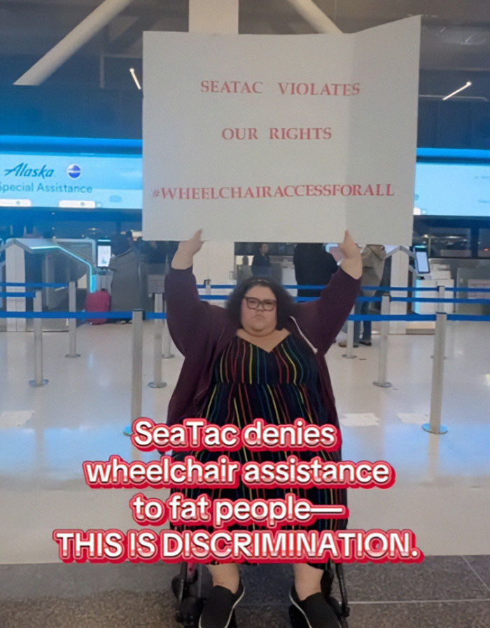 Plus-sized passenger at airport holding sign about wheelchair access rights and discrimination. Plus-sized passenger at airport holding sign about wheelchair access rights and discrimination.