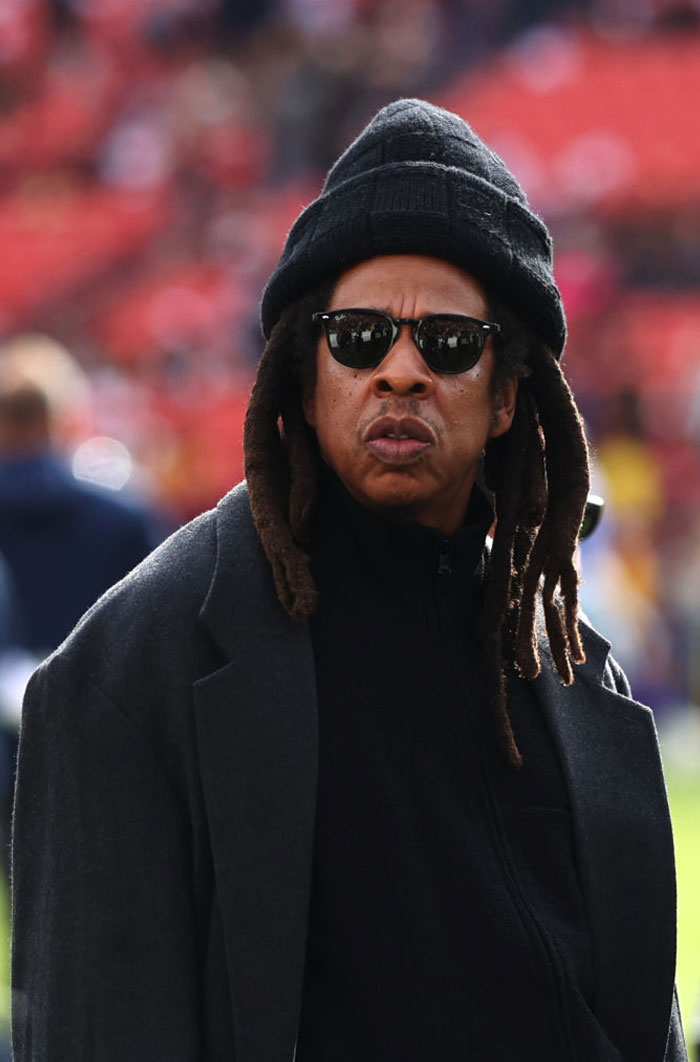 Jay-Z with sunglasses and a hat outdoors, embodying a billion-dollar lifestyle.