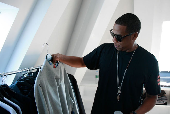 Jay-Z in sunglasses examining clothes, illustrating a billion-dollar lifestyle.